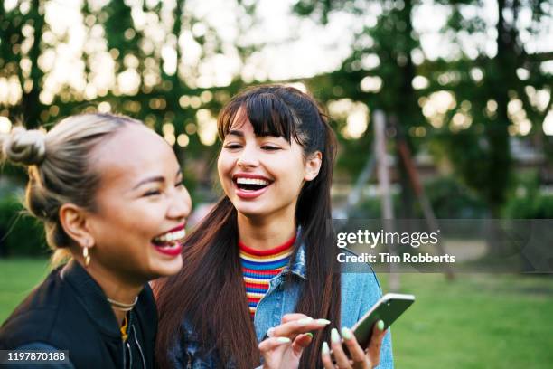 friends laughing with smart phone, city park - friend mischief stock pictures, royalty-free photos & images