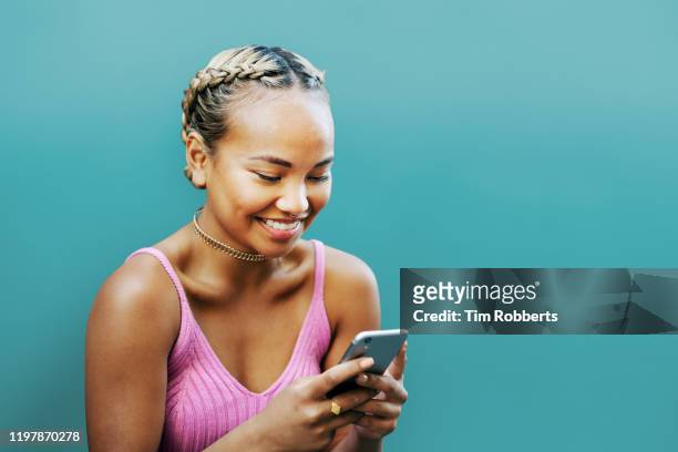 woman smiling with smart phone, blue wall - portrait young colour background cool stockfoto's en -beelden