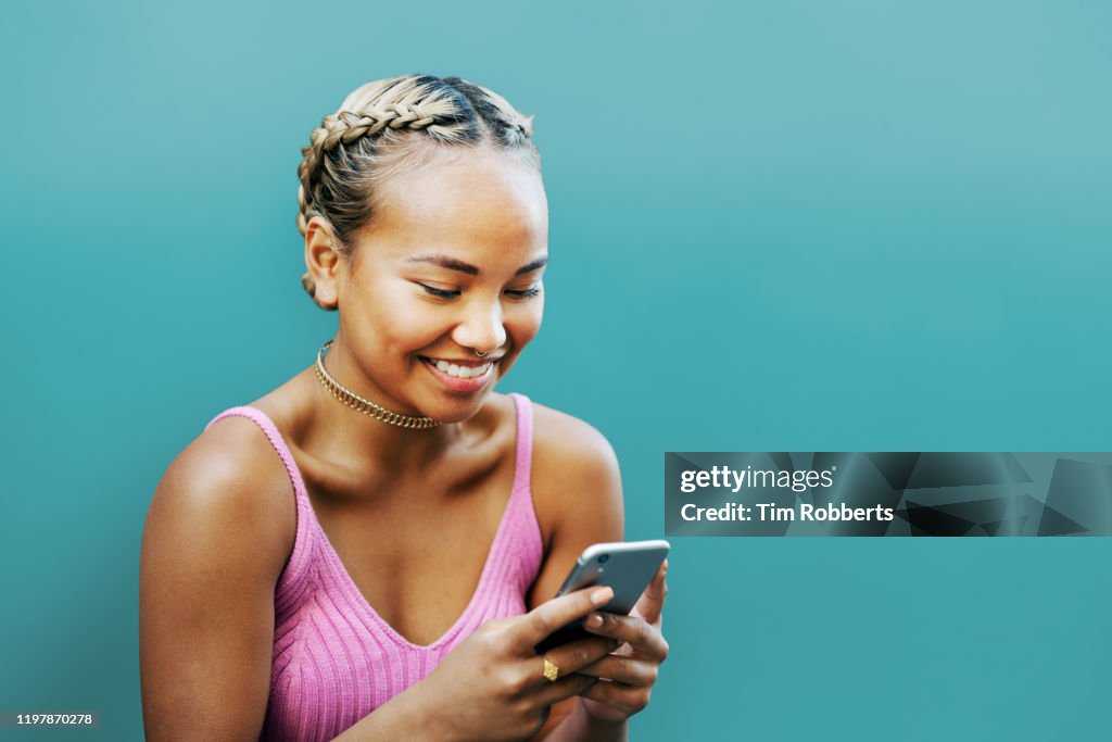 Woman smiling with smart phone, blue wall