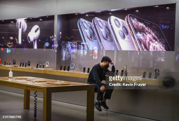 Chinese employee wears a protective mask as he sits in the showroom of an Apple Store after it closed for the day on February 1, 2020 in a shopping...