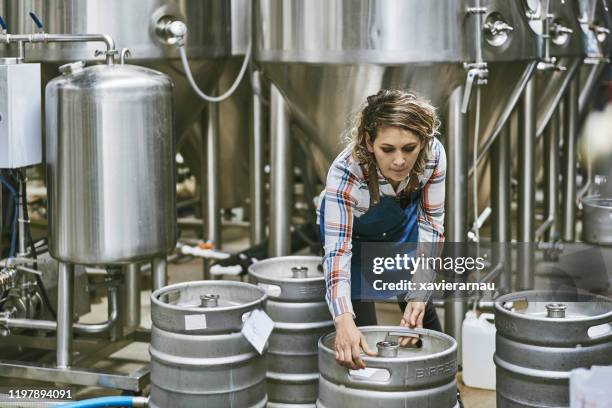 hispanic female brewery worker lifting beer keg - bierfass stock-fotos und bilder