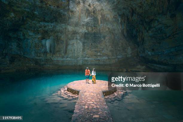 couple holding hands exploring a cenote in yucatan peninsula, mexico - turismo foto e immagini stock