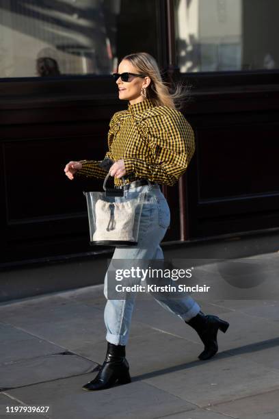 Guest wears a yellow and black check top with puff sleeves, light blue rolled up jeans, perspex bag and black boots during London Fashion Week Men's...