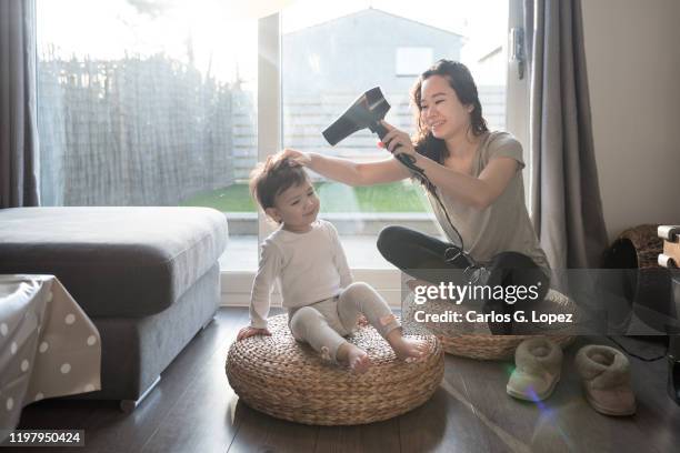 mother dries her daughter's hair with a blow dryer as they sit on wicker stools - drying hair stock pictures, royalty-free photos & images