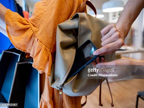 close up shot of female thief trying to steal a smartphone while customer is looking at clothes in a store - thief stock pictures, royalty-free photos & images
