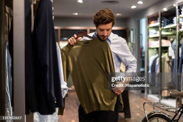 latin american guy trying out a sweater on top at a men's clothing store - vestuário imagens e fotografias de stock