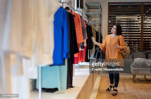ung latinamerikansk kvinna kontrollera klädhängare på en kvinno butik - latin american and hispanic shopping bags bildbanksfoton och bilder