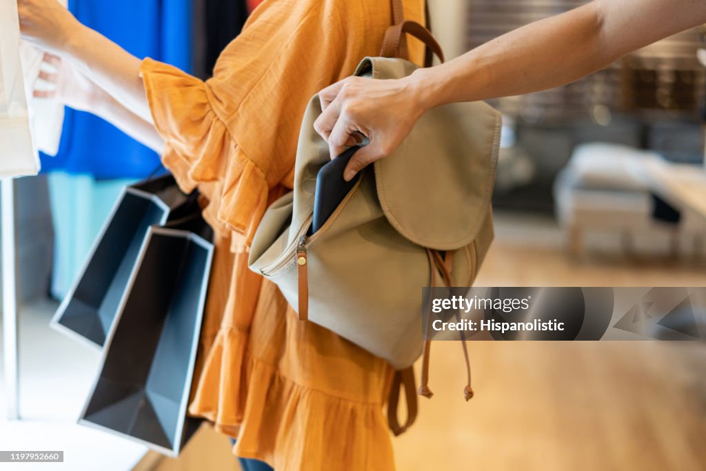 Unrecognizable woman stealing a smartphone from a customers bag at a clothing boutique