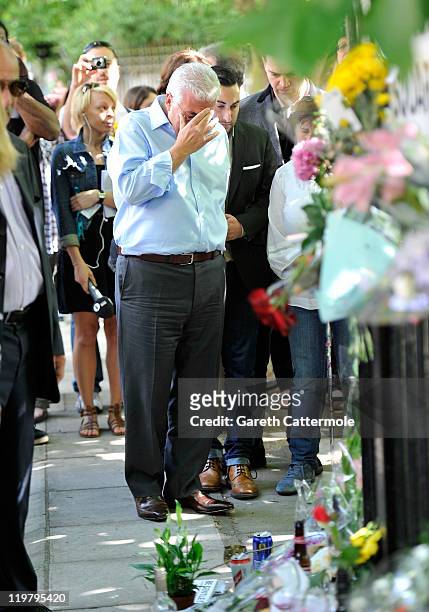 Amy Winehouse's father Mitch Winehouse is comforted by his son, Amy's brother Alex Winehouse as they look at floral tributes left at her house by...