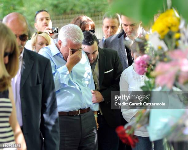 Amy Winehouse's father Mitch Winehouse is comforted by his son, Amy's brother Alex Winehouse as they look at floral tributes left at her house by...