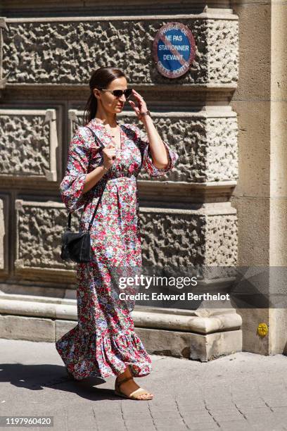 Guest wears sunglasses, a colorful floral print v-neck ruffled long dress, a black bag, sand-color woven leather flat sandals, outside Bode, during...