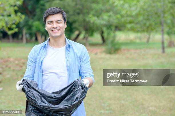 environment protection pollution problems and global warming. young man volunteer holding garbage bag at green park in the big city. - holding garbage bag stock pictures, royalty-free photos & images