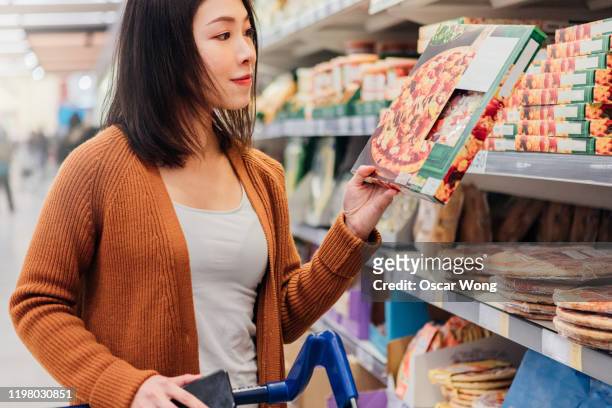 young asian woman picking up pizza in grocery store - comida congelada - fotografias e filmes do acervo