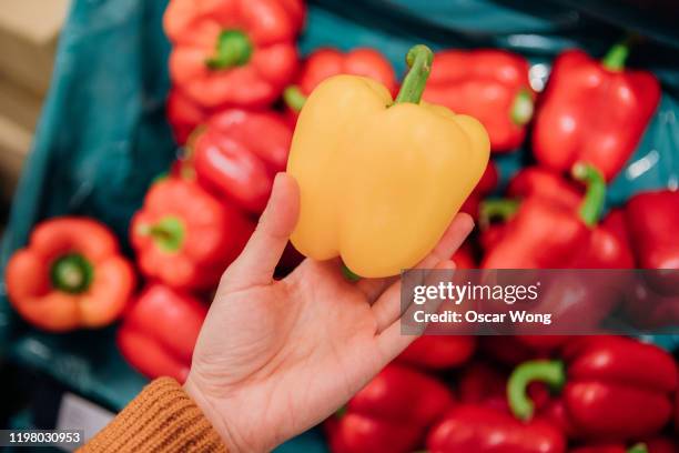 close up shot of woman’s hand holding yellow bell pepper in grocery store - bell pepper stock-fotos und bilder