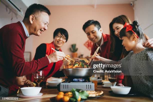 three generations of joyful asian family celebrating chinese new year and enjoying scrumptious traditional chinese poon choi on reunion dinner - shared prosperity stock pictures, royalty-free photos & images