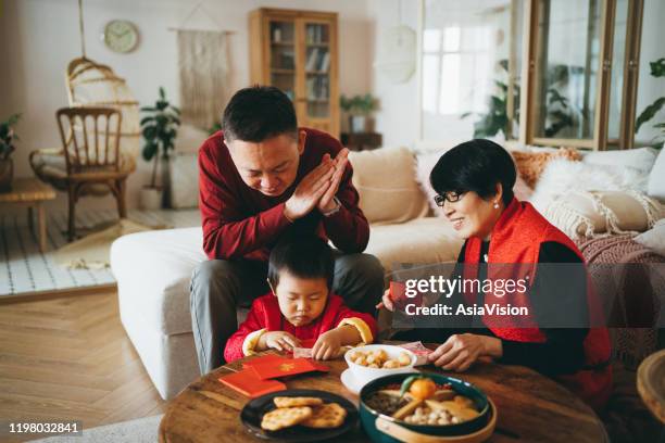 cute little grandson helping his grandparents to prepare red envelops (lai see) at home for chinese new year - kids making money stock pictures, royalty-free photos & images