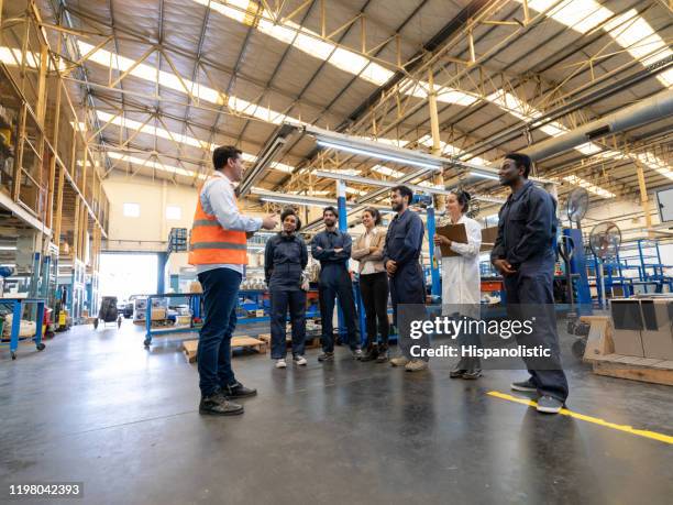 gerente instruyendo a un equipo diverso de ingenieros, trabajadores de cuello azul e inspectores de calidad en una fábrica - protocolo fotografías e imágenes de stock