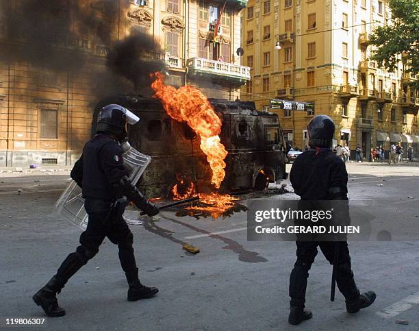 Police officers pass a burning police vehicule during a rally against the G8 summit in Genoa 20 July 2001. One male protestor was killed, one young...