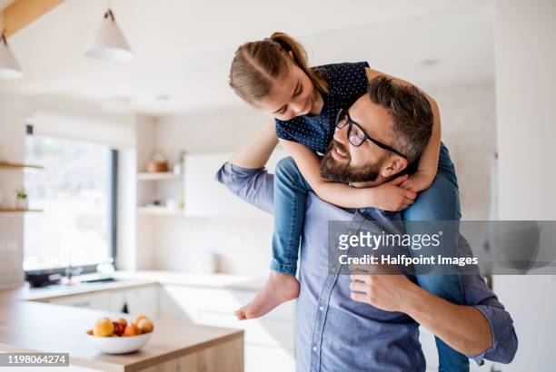 mature father giving piggyback ride to small daughter indoors at home. - offspring stock-fotos und bilder