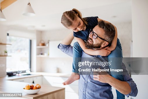 Mature father giving piggyback ride to small daughter indoors at home. Mature father giving piggyback ride to small daughter indoors at home.