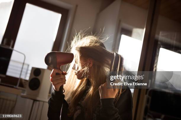 girl (12-13) blow drying her long hair with an electric hairdryer in a bedroom - energie strom stock-fotos und bilder