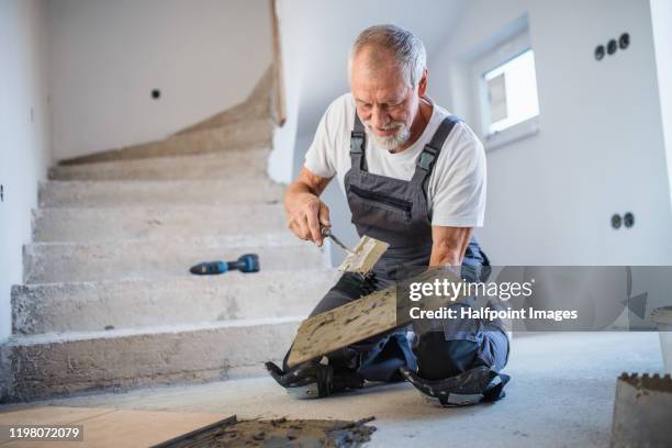 senior man laying tile floor in new home. - flooring installation stock pictures, royalty-free photos & images