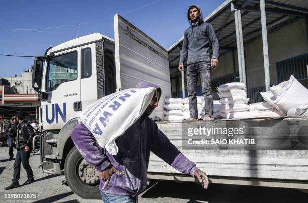 Man transports a sack of flour as people come to receive food aid from a United Nations Relief and Works Agency distribution centre in the Khan Yunis...