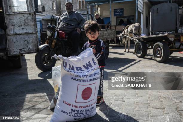 Child stands next to a sack flour as people come to receive food aid from a United Nations Relief and Works Agency distribution centre in the Khan...