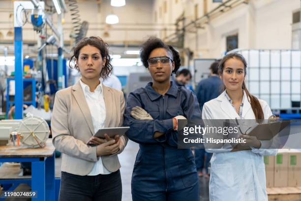 team of powerful women: engineer, supervisor and quality inspector at a factory looking at camera - macacão preto imagens e fotografias de stock