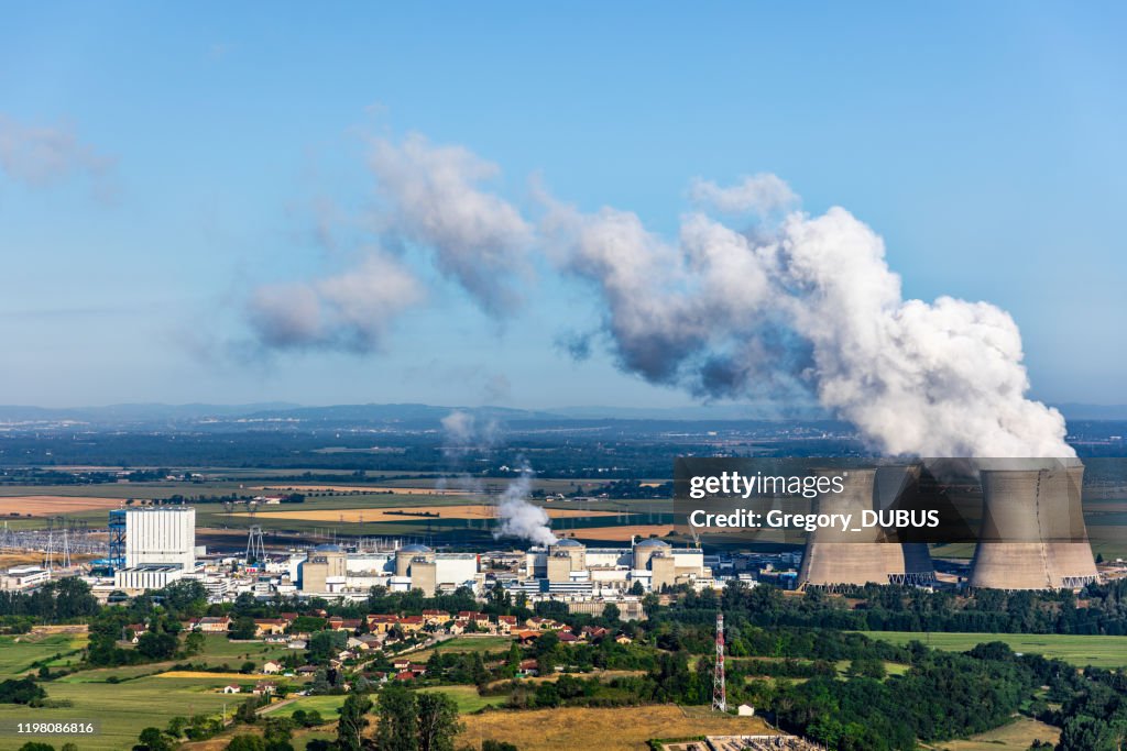 French nuclear power station aerial view in countryside landscape in summer with smoking cooling towers on blue sky