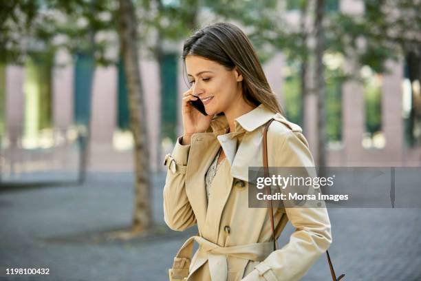 beautiful businesswoman talking on smart phone - trench coat stockfoto's en -beelden