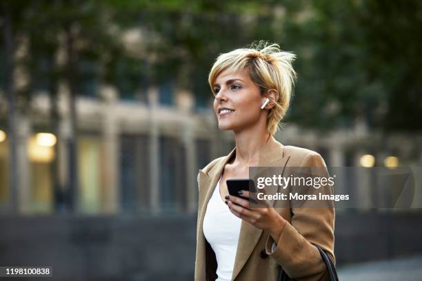 beautiful young businesswoman holding smart phone - in ear headphones photos et images de collection