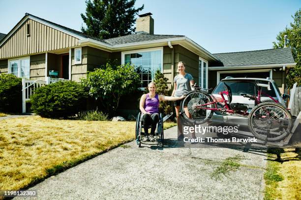 Portrait of female wheelchair athlete and assistant standing at back of car loaded with adaptive mountain bike