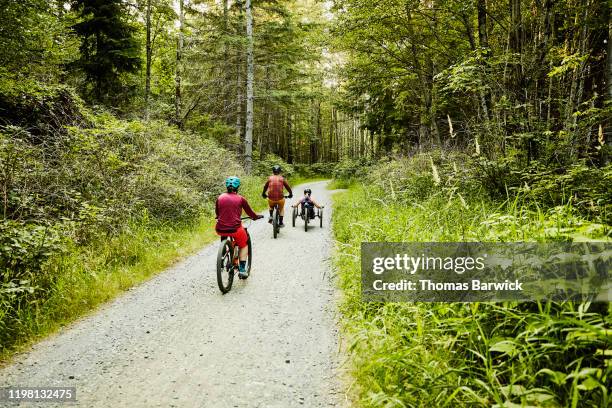 female wheelchair athlete riding adaptive mountain bike up trail with friends - athlete bulges stock pictures, royalty-free photos & images