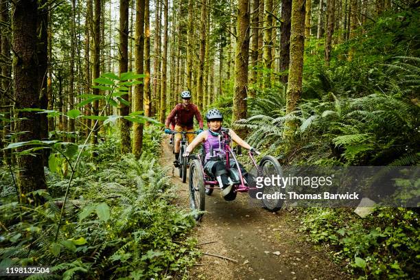 female wheelchair athlete riding adaptive mountain bike on trail with friend - frau rollstuhl selbstständigkeit stock-fotos und bilder