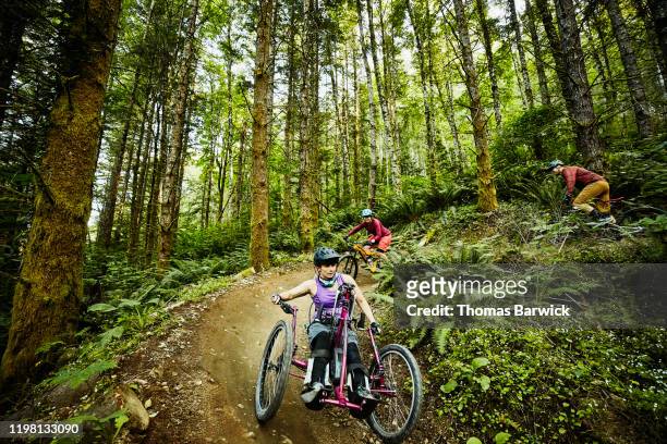 female wheelchair athlete riding adaptive mountain bike on trail with friend - disabilitycollection stock pictures, royalty-free photos & images