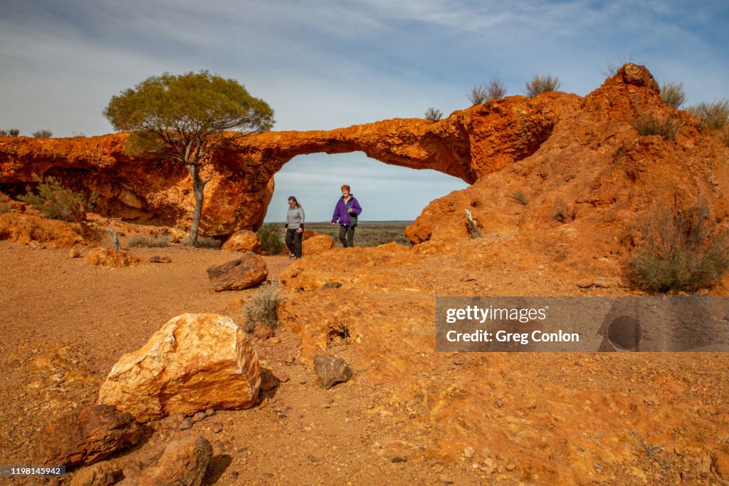 Two senior ladies walking under the London Bridge rock formation. Sandstone, WA, Australia