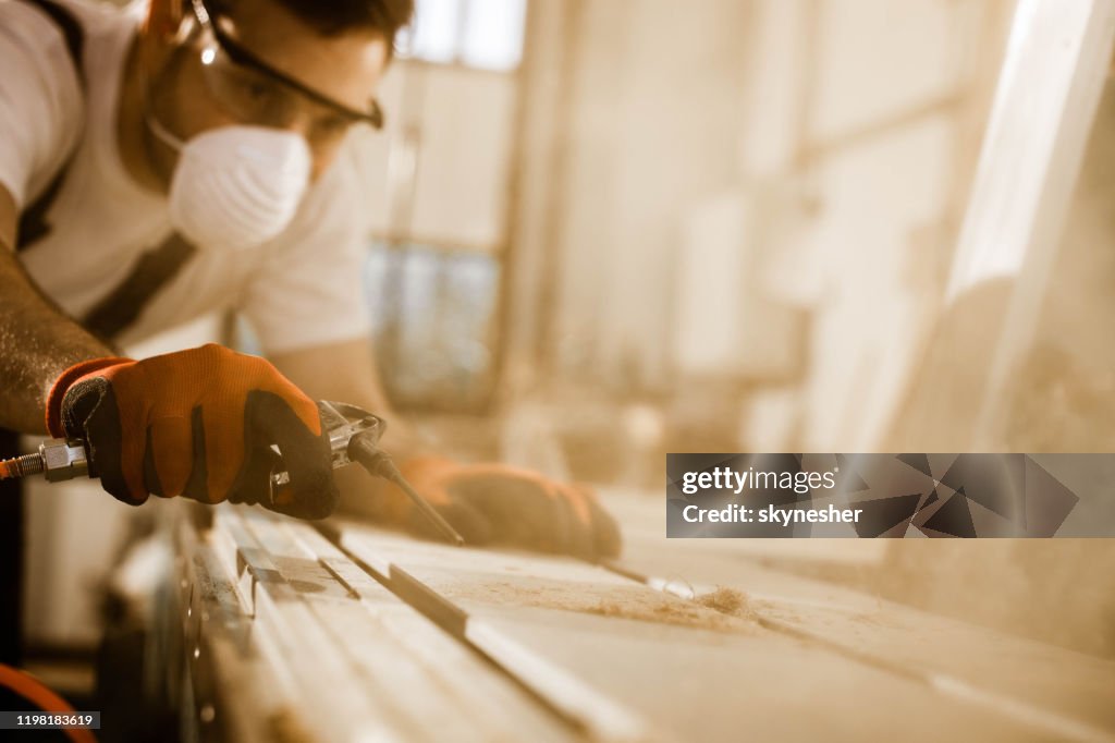 Close up of carpenter using air pump to blow sawdust from a plank.