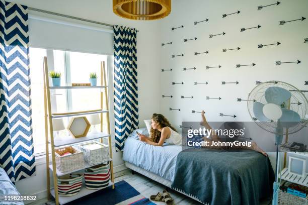 jeune fille hispanique se trouvant sur le lit utilisant le téléphone intelligent - allongé sur le devant photos et images de collection