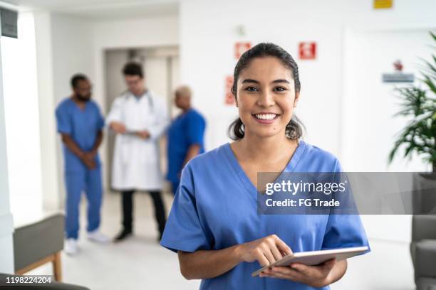 portrait of female nurse using tablet at hospital - female nurse scrubs stock pictures, royalty-free photos & images