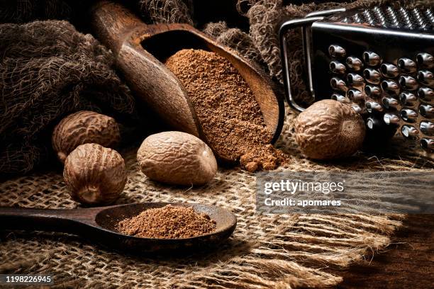close-up of whole nut and nutmeg powder in a wooden spoon with  on burlap and rustic table - nutmeg stock pictures, royalty-free photos & images
