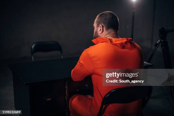 male prisoner in orange jumpsuit sitting alone in interrogation room - prison jumpsuit stock pictures, royalty-free photos & images