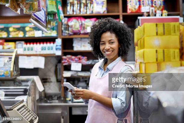 lachende vrouwelijke eigenaar met smart phone in de winkel - caissière stockfoto's en -beelden