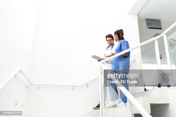 doctor and nurse walking down the stairs and talking at hospital - doctor looking down stock pictures, royalty-free photos & images