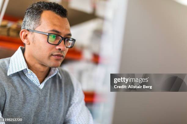 manager checking stock on a computer in a busy small warehouse - busy warehouse stock pictures, royalty-free photos & images