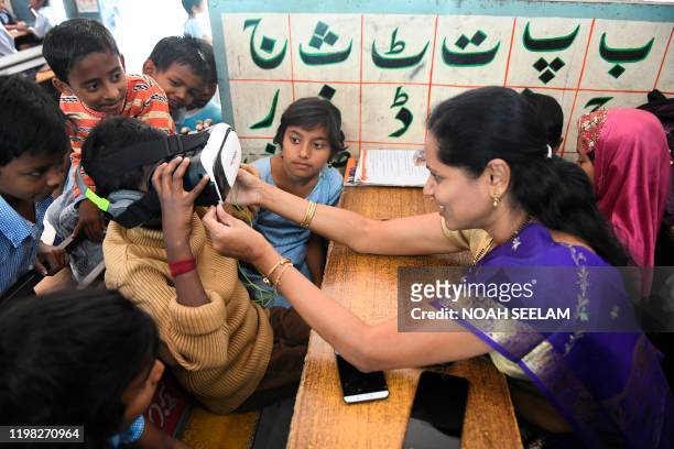Teacher helps a student to try a virtual reality headset, introduced in the class to increase the students attention span, at a government primary...