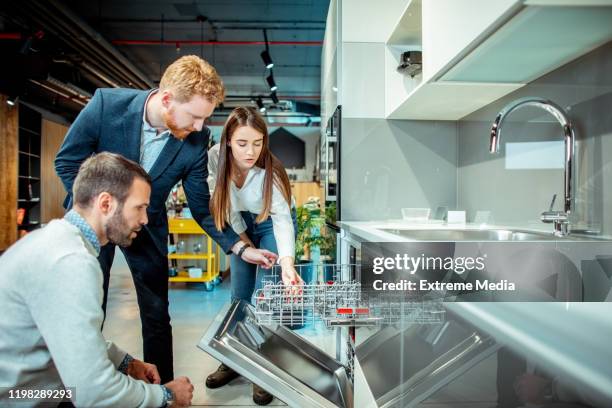 winkel verkoper die de kenmerken en functionaliteit van een vaatwasser aan een jonge man en vrouw in een keuken apparatuurwinkel toont - buying washing machine stockfoto's en -beelden