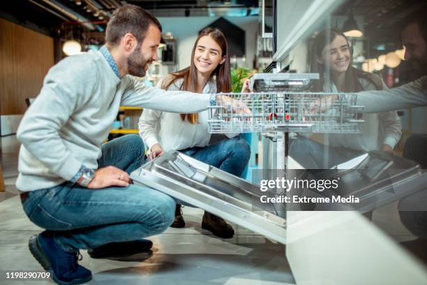 husband and wife shopping for a new dishwasher model to a young shopping couple in a kitchen appliances store - department store stock pictures, royalty-free photos & images