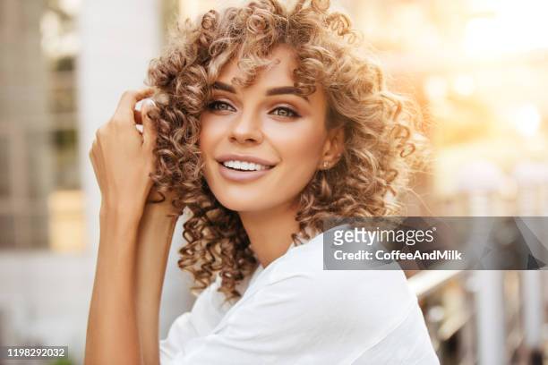 陽気なブロンドの女性は、美しい夕日の間に笑顔で屋外で楽しんでいます - curly hair ストックフォトと画像