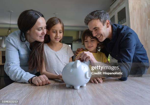 loving latin american parents teaching their kids to save money in a piggy bank - family budget imagens e fotografias de stock